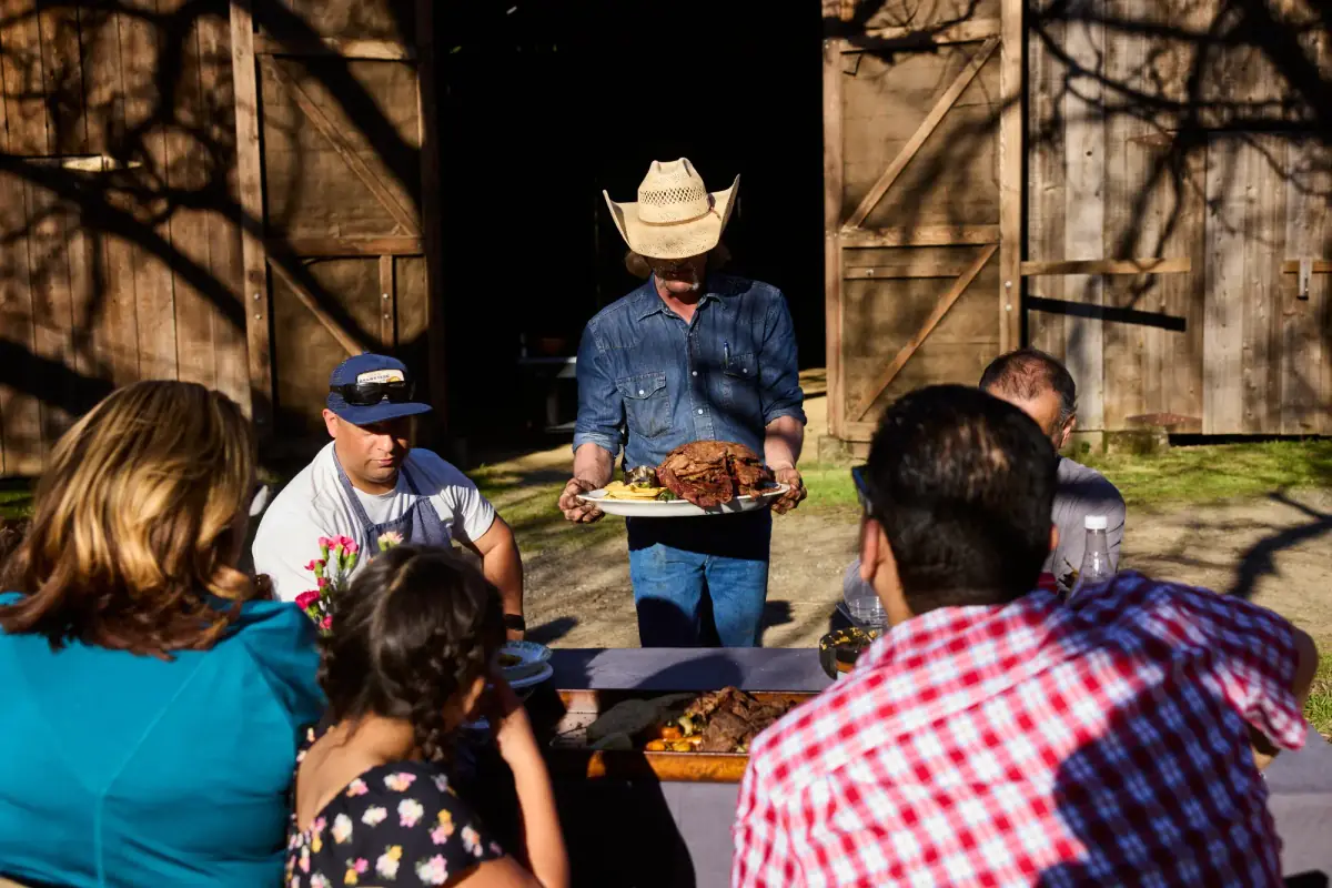 La familia de Spanglish Asadero reunida a la mesa en el rancho, con la carne recién salida de la parrilla.